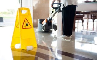 A worker cleaning a floor with a wet floor sign in place, working for contract cleaning services that provide consistent multi-site cleans.